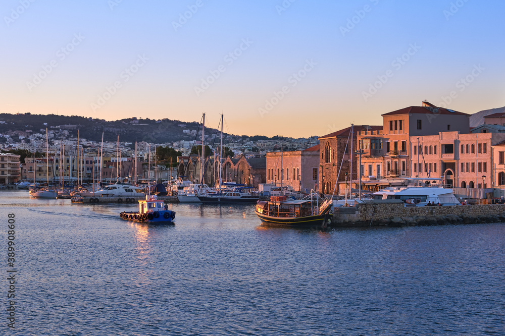Fishing boat leaving Old Venetian port of Chania, Crete, Greece at sunrise. Sailboats, yachts, Grand Arsenal, Old Venetian shipyards or Neoria 