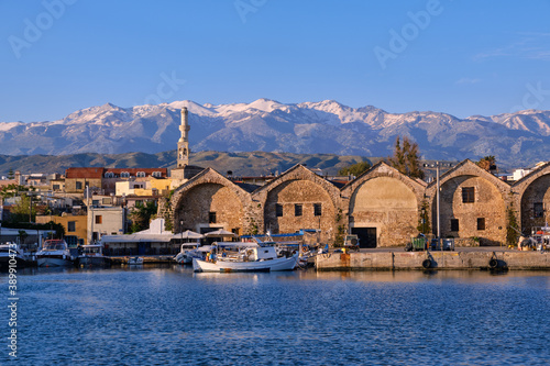 Fishing boats anchored by piers of Old Venetian shipyards or Neoria. Church bell tower and minaret, distant Cretan mountain. Chania, Crete, Greece. photo