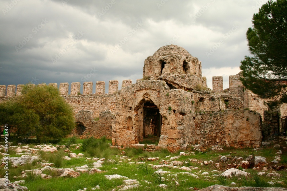 Old ruins of medieval castle surrounding walls and a church inside. Abandoned historic place under dramatic cloudy sky. 