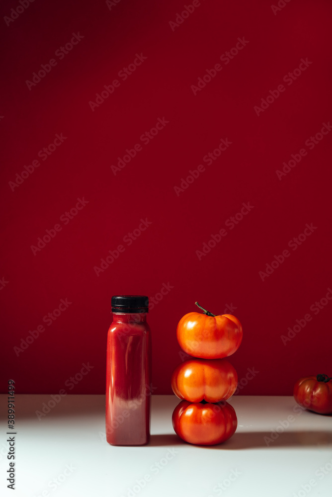 Red smoothie drink in bottle surrounded bY tomatoes and beets on red background Red smoothie drink in bottle surrounded bY tomatoes and beets on red background