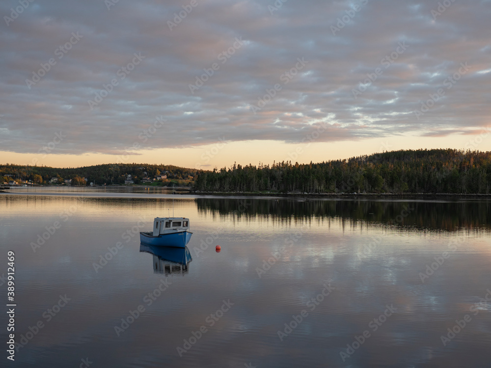 Fishing boat in a bay floating on mirror like sea at sunset