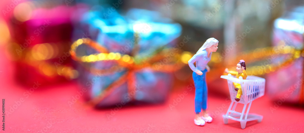 Miniature people with new year and Christmas holiday ornament in background. Holiday shopping concept is banner size
