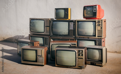 Piles of old vintage televisions on cement floor, outdoors.