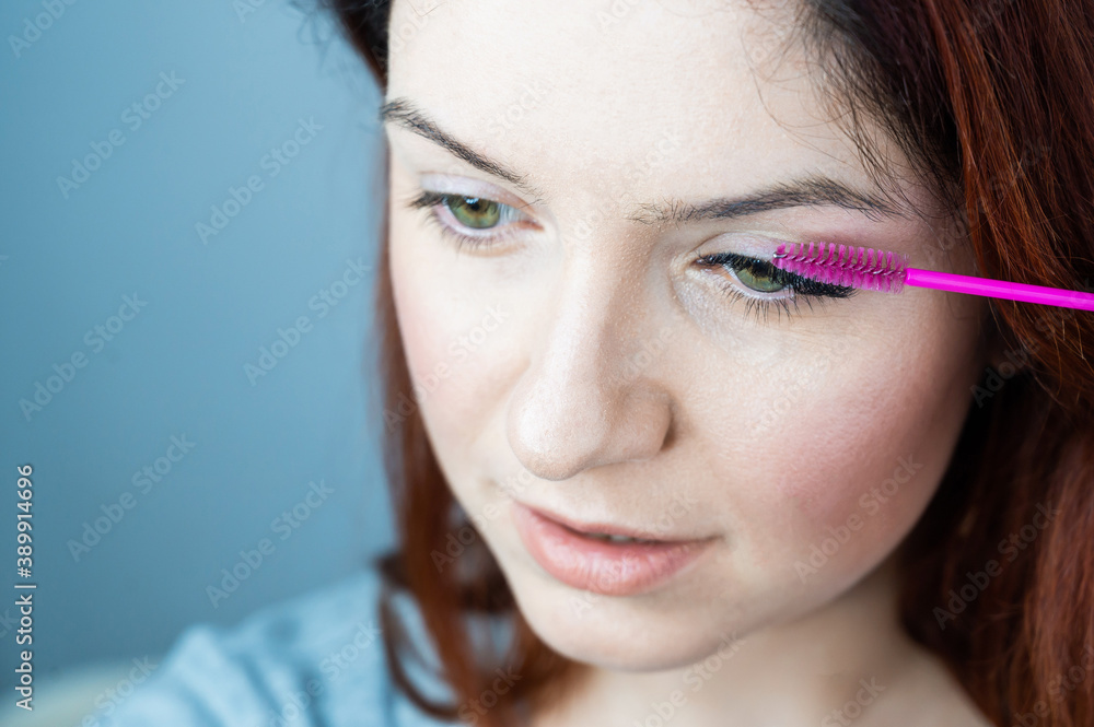 Red head woman brushing her extension eyelashes with a brush. girl with impending eyelid make-up mascara. Beauty industry. Red head woman brushing her extension eyelashes with a brush. girl with impending eyelid make-up mascara. Beauty industry.