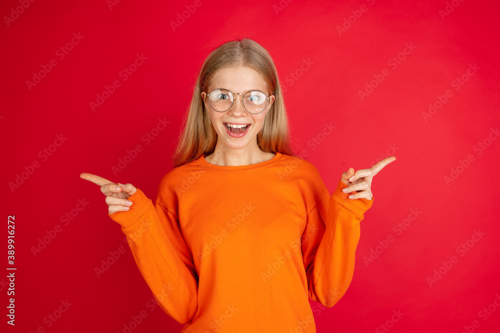 Pointing. Portrait of young caucasian woman isolated on red studio background with copyspace. Beautiful female model. Concept of human emotions, facial expression, sales, advertising, youth. Pointing. Portrait of young caucasian woman isolated on red studio background with copyspace. Beautiful female model. Concept of human emotions, facial expression, sales, advertising, youth.