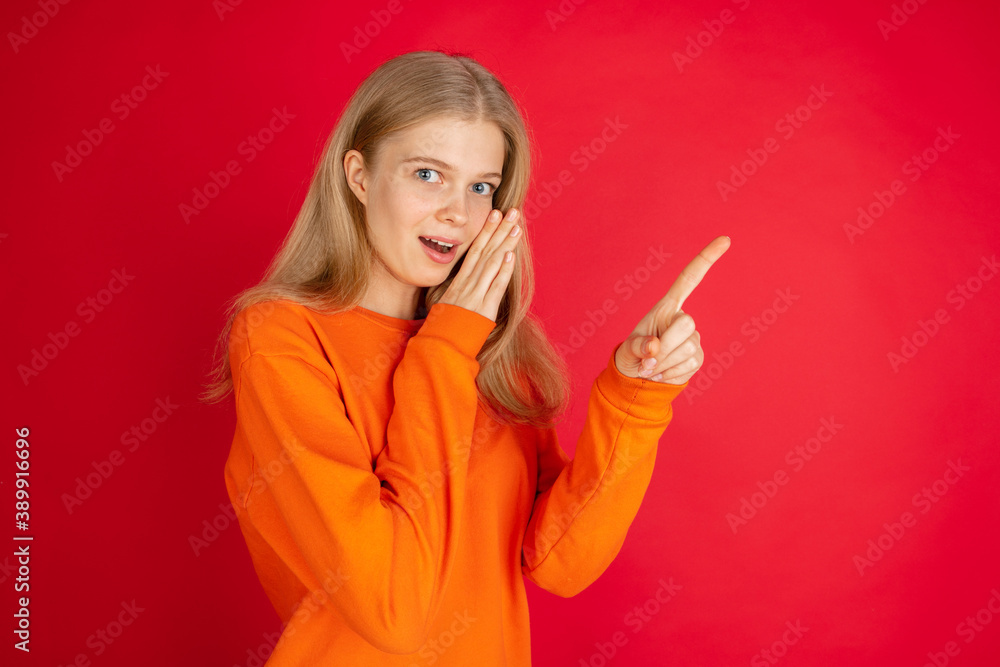 Pointing. Portrait of young caucasian woman isolated on red studio background with copyspace. Beautiful female model. Concept of human emotions, facial expression, sales, advertising, youth. Pointing. Portrait of young caucasian woman isolated on red studio background with copyspace. Beautiful female model. Concept of human emotions, facial expression, sales, advertising, youth.