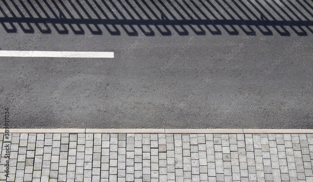Fototapeta premium Detail of promenade road with bicycle lane, pedestrian sidewalk and shadow of a fence