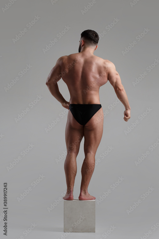 Young muscular man of athletic build isolated on gray background view from the back.