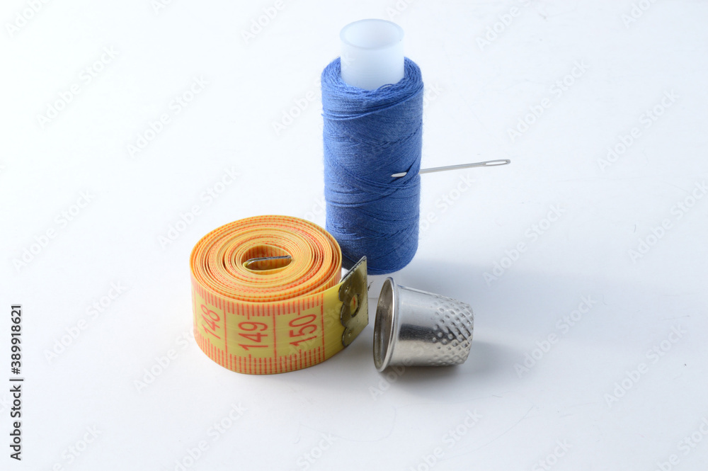 thimble, needle with thread and measuring tape on a white background .close-up. thimble, needle with thread and measuring tape on a white background .close-up.