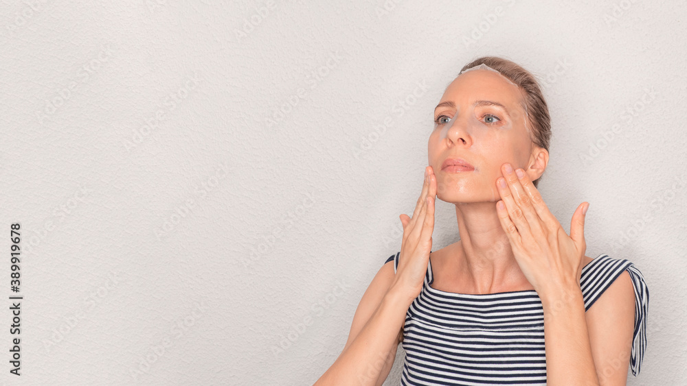 Face care and beauty treatments. Middle age woman with a cloth moisturizing mask on her face on a light background. Face care and beauty treatments. Middle age woman with a cloth moisturizing mask on her face on a light background.