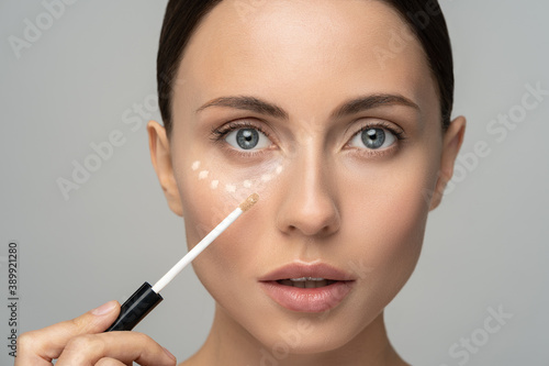 Close up of woman with natural makeup applying corrector on flawless fresh skin, doing make up. Girl after shower put concealer under eye area. Beauty face, skin care. Copy space, banner, advertising. photo