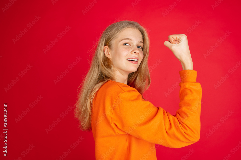 Fototapeta premium Strong, power. Portrait of young caucasian woman isolated on red studio background with copyspace. Beautiful female model. Concept of human emotions, facial expression, sales, ad, youth.