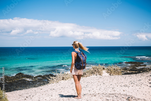 Tableau sur toile Young female traveller with touristic backpack admire seascape views enjoying su