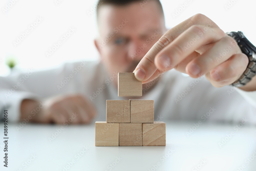 Man builds pyramid from wooden cubes in office. Small and medium business development concept Man builds pyramid from wooden cubes in office. Small and medium business development concept