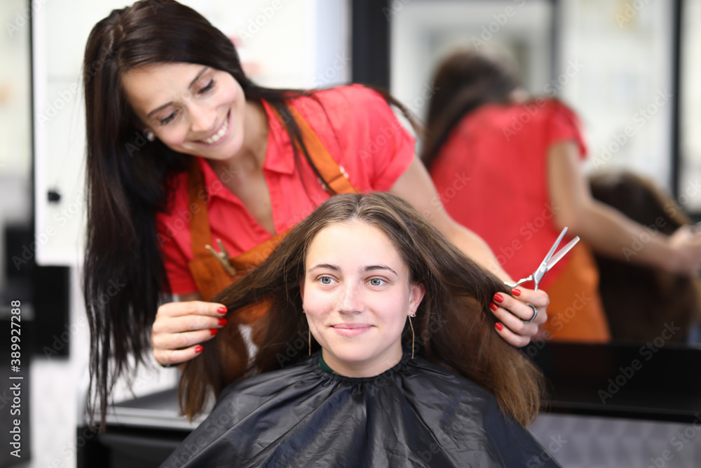 Smiling female master hairdresser holds hair of client and scissors in hands. Hairdresser training and courses concept