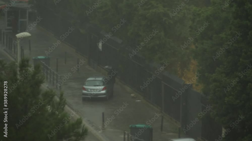 Woman with a black umbrella walking in the street during a tempest with heavy rain next to a bus stop in Marseille, France