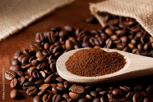 coffee powder (ground), on wooden spoon, coffee beans, with raffia cloth bag, brown background