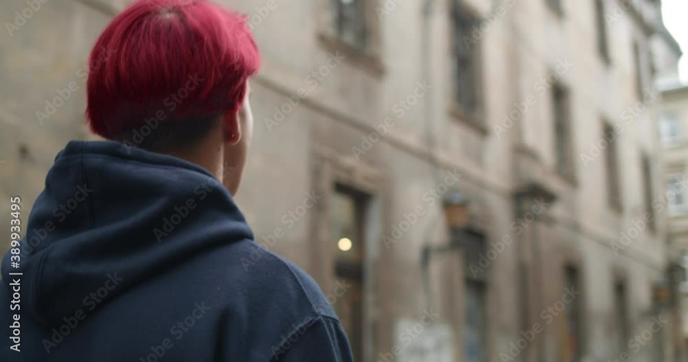 Backside view of young man with dyied red hair looking around while walking at old city street. Millennial hipster guy traveling to another city. Concept of tourism and people. Backside view of young man with dyied red hair looking around while walking at old city street. Millennial hipster guy traveling to another city. Concept of tourism and people.