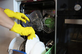 Man in yellow gloves takes out dishes from dishwasher. House cleaning staff recruitment concept