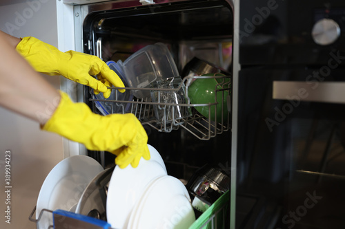 Man in yellow gloves takes out dishes from dishwasher. House cleaning staff recruitment concept