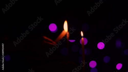 Person's hand illuminating or lighting up the candles in a row at night in a decorative festive background. Diwali celebration, holiday, festive rituals, grief, prayer.