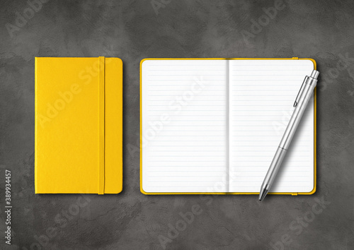 Yellow closed and open lined notebooks with a pen on dark concrete background