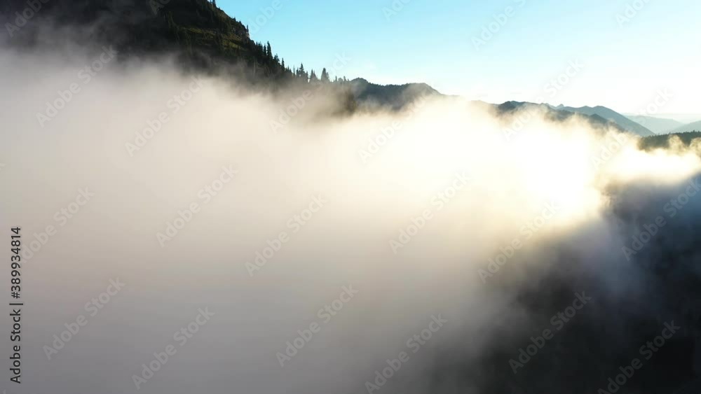 Flying Into Low Clouds in Mountain Valley Under Golden Hour Sunlight on Summer. Aerial View of Landscape and Weather Conditions in Mount Rainier, Washington State USA Flying Into Low Clouds in Mountain Valley Under Golden Hour Sunlight on Summer. Aerial View of Landscape and Weather Conditions in Mount Rainier, Washington State USA