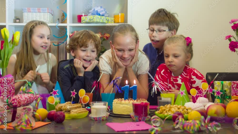 Make a Wish and Blow Out the Candles. A birthday girl at a festive table surrounded by friends who joyfully demand to blow out the candles on the cake Make a Wish and Blow Out the Candles. A birthday girl at a festive table surrounded by friends who joyfully demand to blow out the candles on the cake