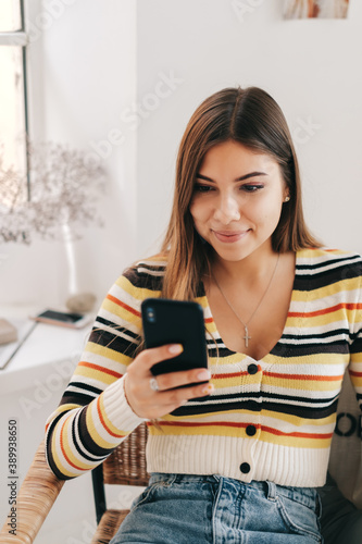 Attractive young caucasian woman use smartphone, sitting on armchair in bright living room.