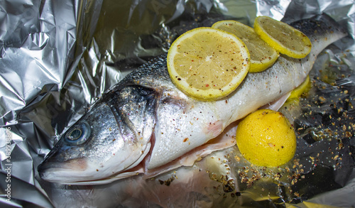Fresh sea bass with lemon and spices on aluminum foil.