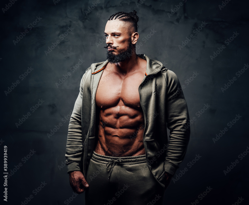 Powerful bodybuilder with dreadlocks and moustache in gray sportswear poses with serious face in dark background. Powerful bodybuilder with dreadlocks and moustache in gray sportswear poses with serious face in dark background.