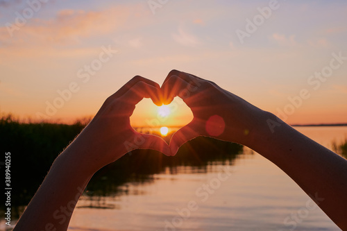 child is forming a heart around the sun  in front of the lake Chiemsee during sunset