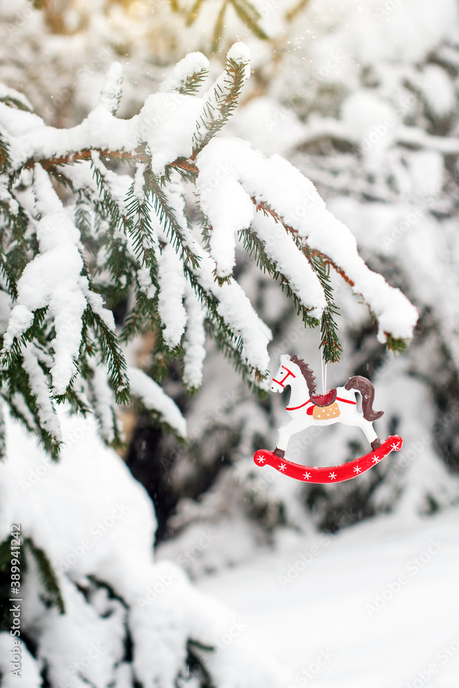 Toy horse on a snow-covered fir branch. Christmas tree in the snow and Christmas decorations. Christmas card.