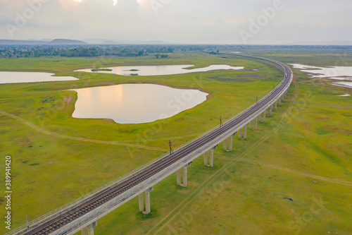 Aerial view of Thai local train on railway bridge at Pa Sak Jolasid Dam, the biggest reservoir in central Thailand, in Lopburi province with cloudy sky in transportation and travel concept. photo