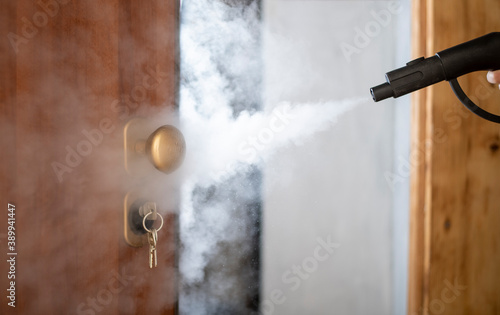 disinfection and sanitization with steam at home, steam flow is directed to the door handle and keys in the lock photo