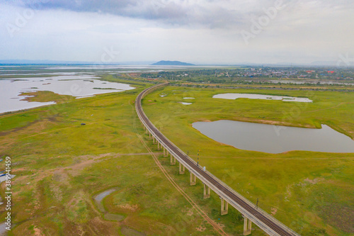 Aerial view of Thai local train on railway bridge at Pa Sak Jolasid Dam, the biggest reservoir in central Thailand, in Lopburi province with cloudy sky in transportation and travel concept. photo