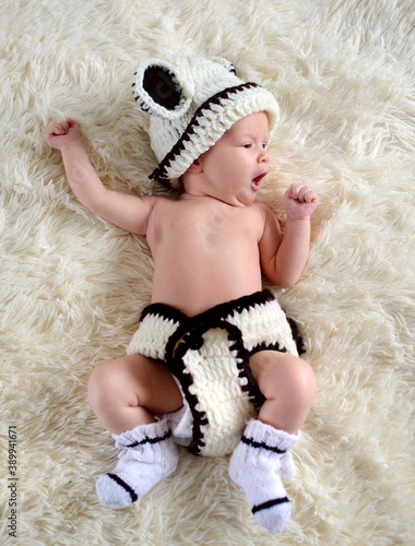 Newborn baby in a knitted suit yawns while lying on a fur blanket. Beautiful portrait of a small child, two weeks ago.