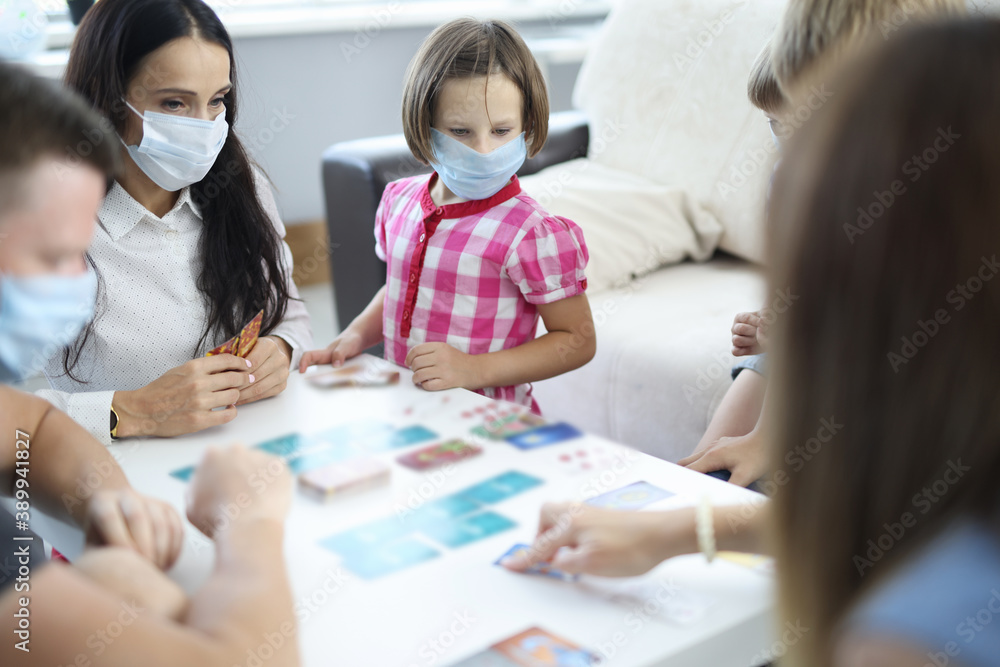 Adults and children in medical protective masks play board games. Safe health games in pandemic concept Adults and children in medical protective masks play board games. Safe health games in pandemic concept