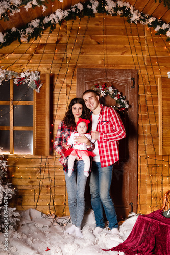 Mom and dad pose with their charming little daughter in decorated christmas studio. New Year photo session.