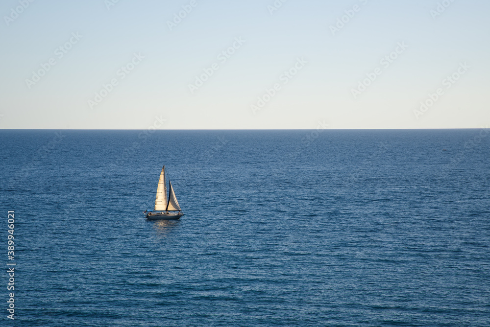 Single sailboat on a calm sea in the late afternoon; blue background with copy space