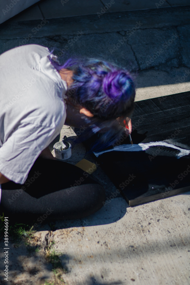 Latin hispanic woman with colorful hair painting a wooden board with black and white paint. Outdoors painting hobbie Latin hispanic woman with colorful hair painting a wooden board with black and white paint. Outdoors painting hobbie