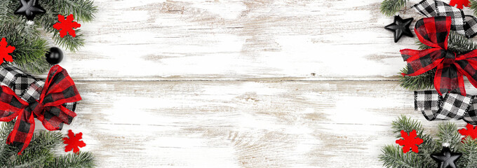 Christmas double border of ornaments, branches and checked buffalo plaid ribbon. Above view on a rustic white wood background.