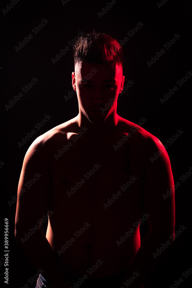 Fototapeta premium Young adult illuminated by red and white lights with a black background.