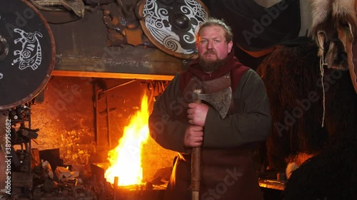 Portrait of medieval viking. Man is looking at camera, dressed in medieval clothes, near shield and axe photo