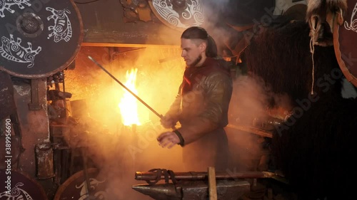 The medieval viking taken sword to examine metal of sword on background of blacksmith's forge photo