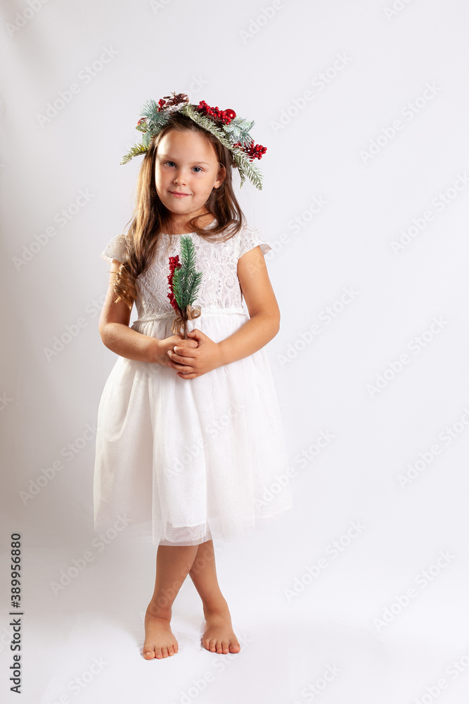 full-length portrait of a girl in a white Princess dress and a Christmas wreath, barefoot, isolated on a blue background.