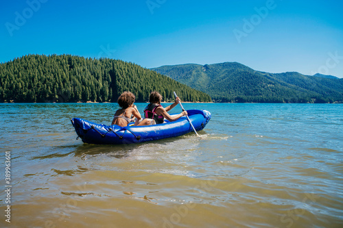 Sisters paddling inflatable kayak on lake water in forest