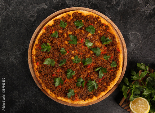 Turkish cuisine. Lahmacun. Turkish round pizza with minced meat, tomatoes, sweet peppers, onions, herbs and lemon on a wooden board on a black table. Background image, copy space, flatlay, top view