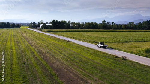 Aerial shot of a small truck driving on a rural road with farming fields.