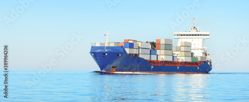 Large cargo container ship sailing in an open sea on a clear day. Panoramic view. Freight transportation, global communications, logistics, industry, business, economy, environmental damage © Alex Stemmer